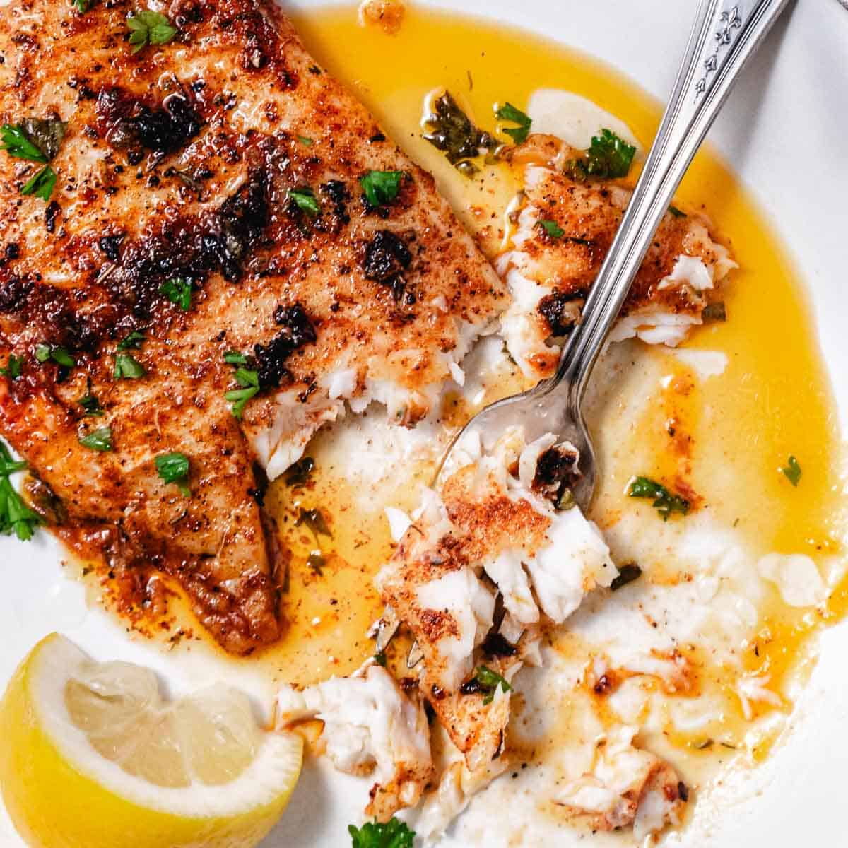 Blackened fish flaking with a fork in lemon butter sauce.