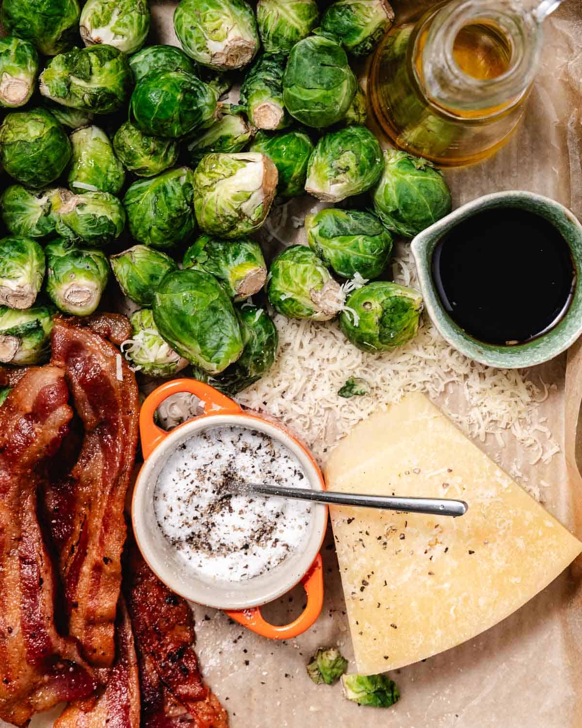Overhead view of trimmed Brussels sprouts, strips of bacon, grated Parmesan, and balsamic ready for cooking.