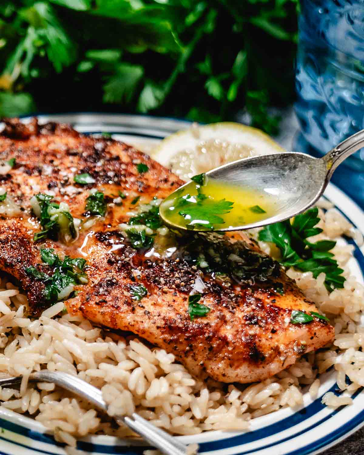 Spoonful of lemon butter sauce being poured over a blackened fish fillet.