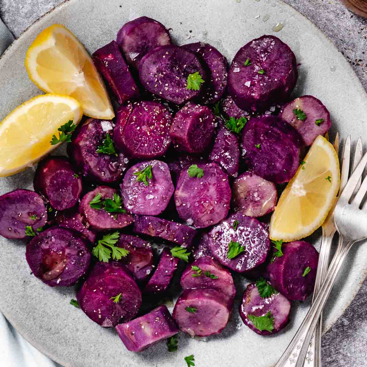 overhead view of plate of steamed purple sweet potatoes with lemon wedges, olive oil, salt and pepper
