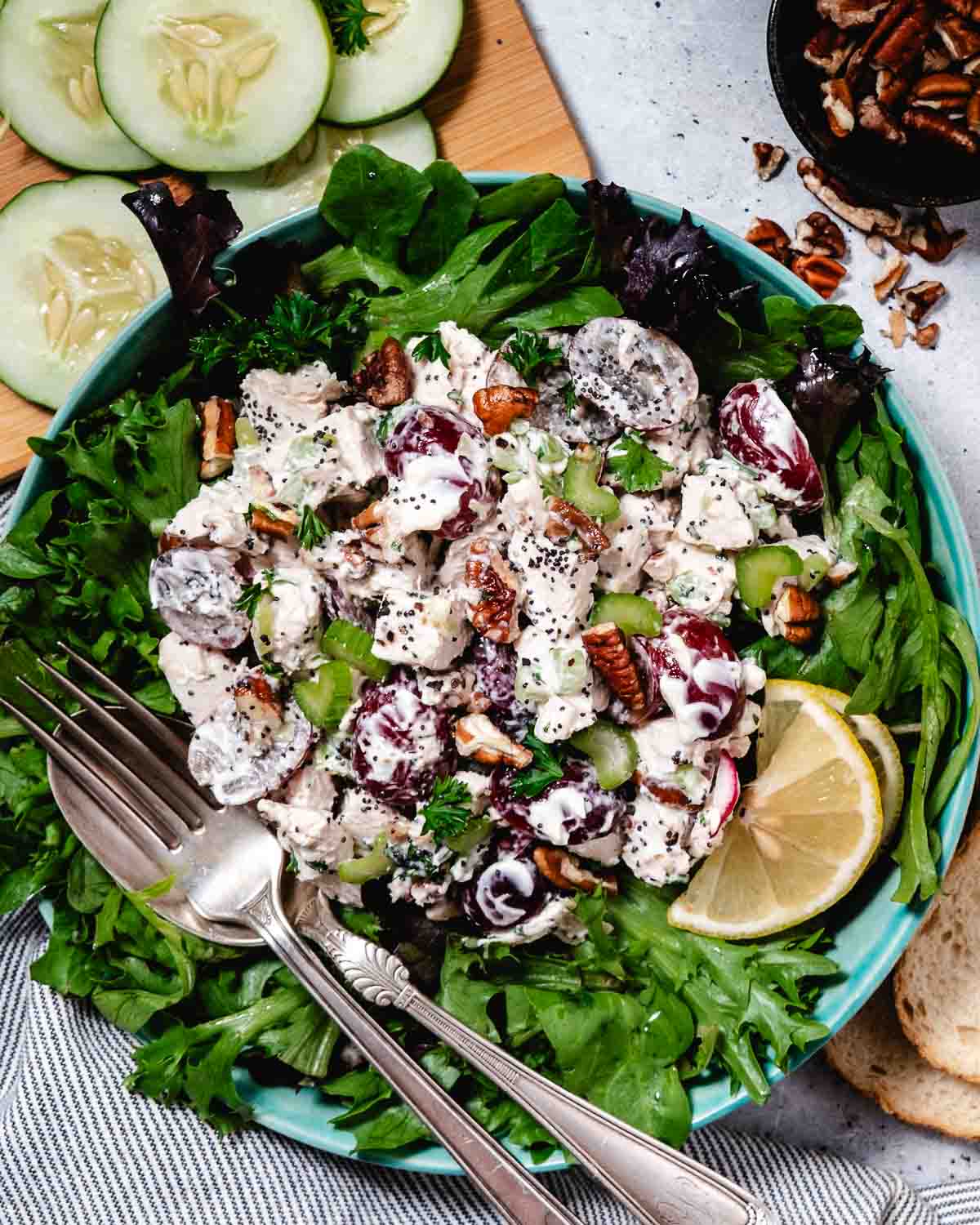 Bowl of Sonoma chicken salad with grapes, celery, pecans, and poppyseed dressing served over mixed greens with lemon slices.