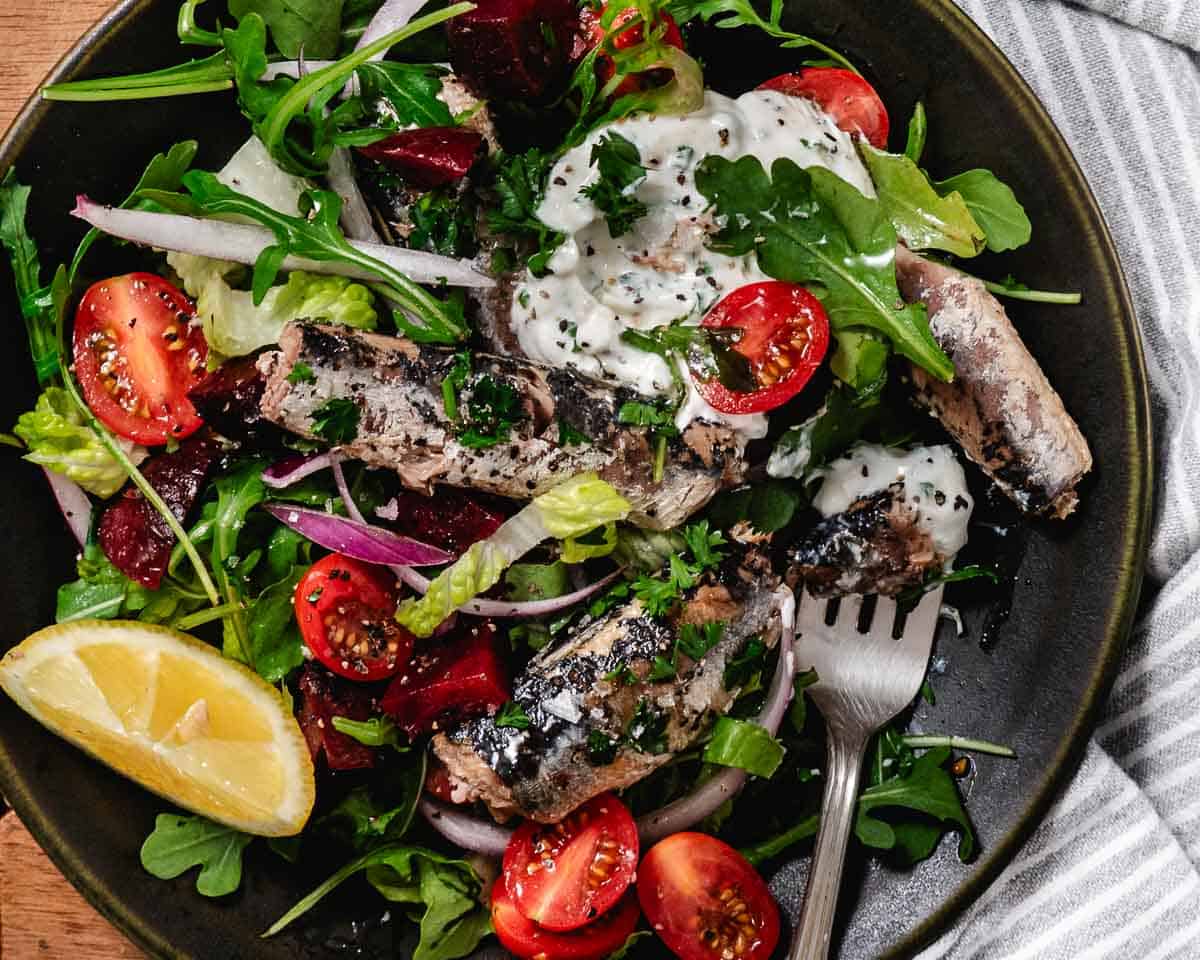 Canned sardines on a green salad with arugula, romaine, tomatoes, and creamy garlic dressing