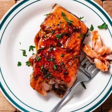 Honey-garlic glazed salmon on a white plate. The fillet is topped with a sauce and chopped parsley.