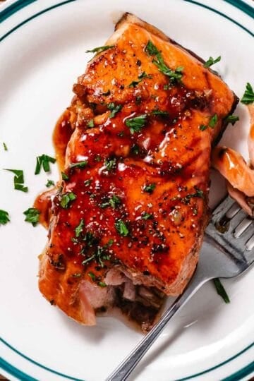 Honey-garlic glazed salmon on a white plate. The fillet is topped with a sauce and chopped parsley.