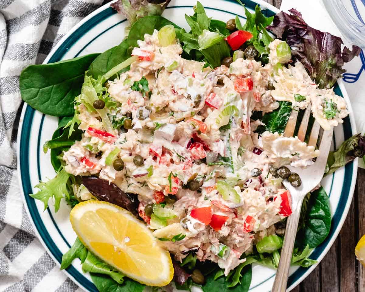 Overhead view of creamy salmon pasta salad with bowtie pasta, flaked salmon, fresh dill, scallions, and lemon wedges in a white bowl.