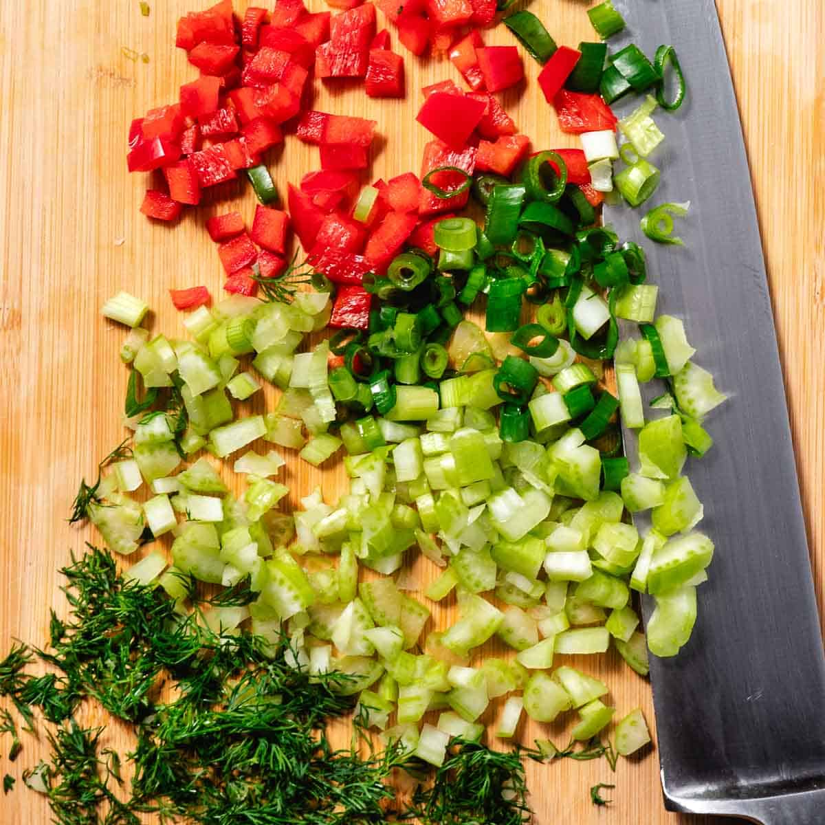 Overhead view of chopped vegetables and herbs: red bell peppers, spring onions, celery, and dill.