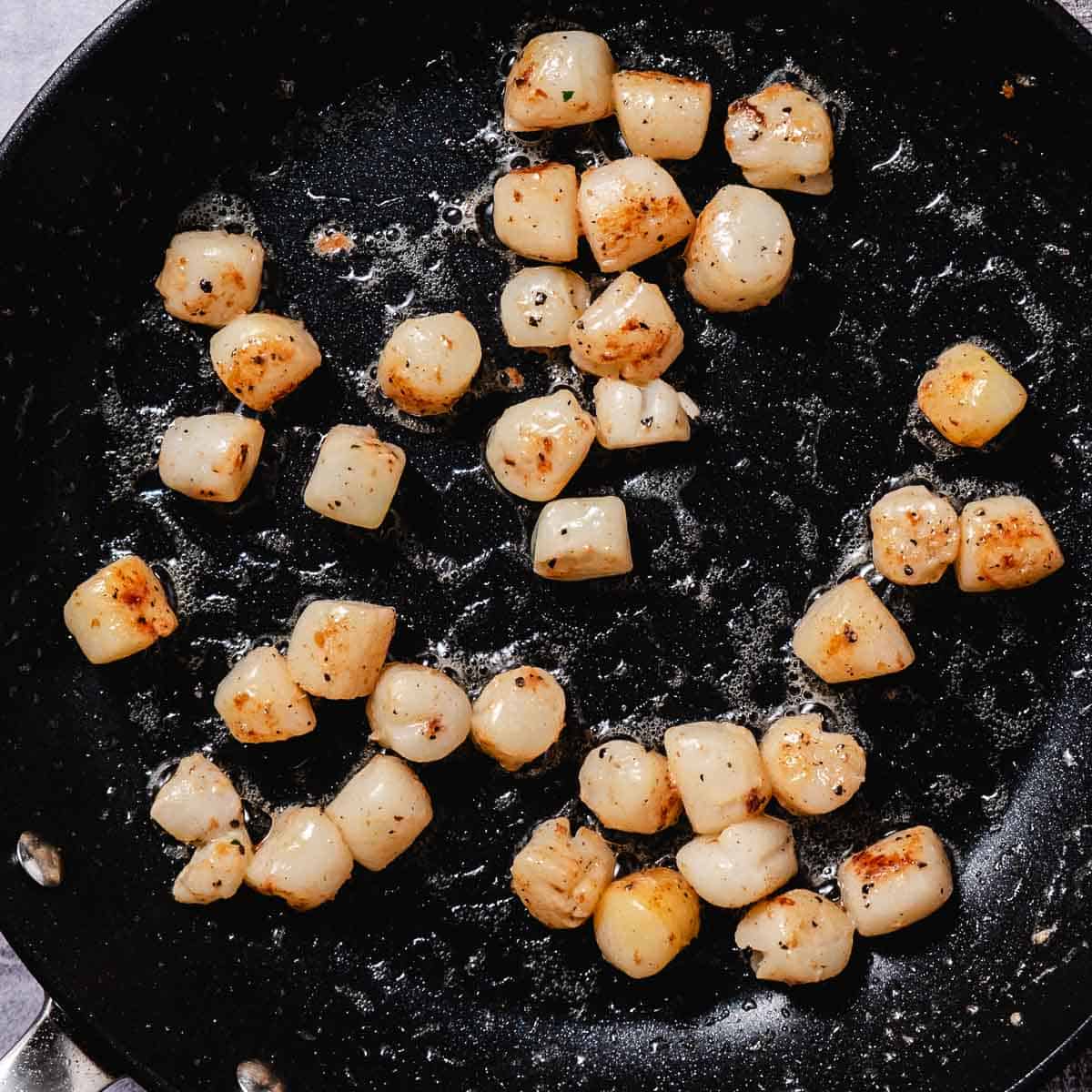 Bay scallops searing in a single layer in a hot skillet.