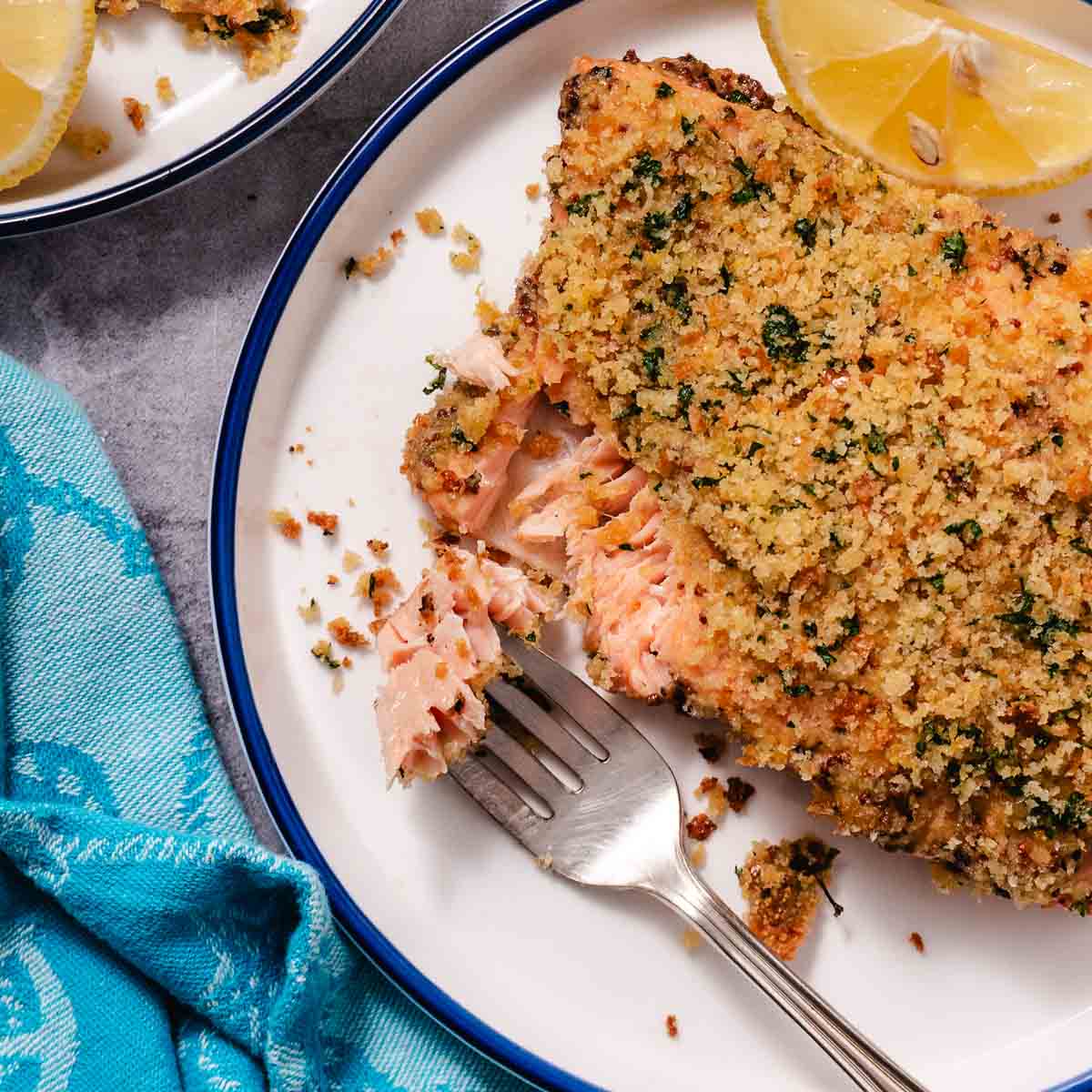 Close-up of baked salmon with a breadcrumb crust, flaked with a fork to show the tender center.