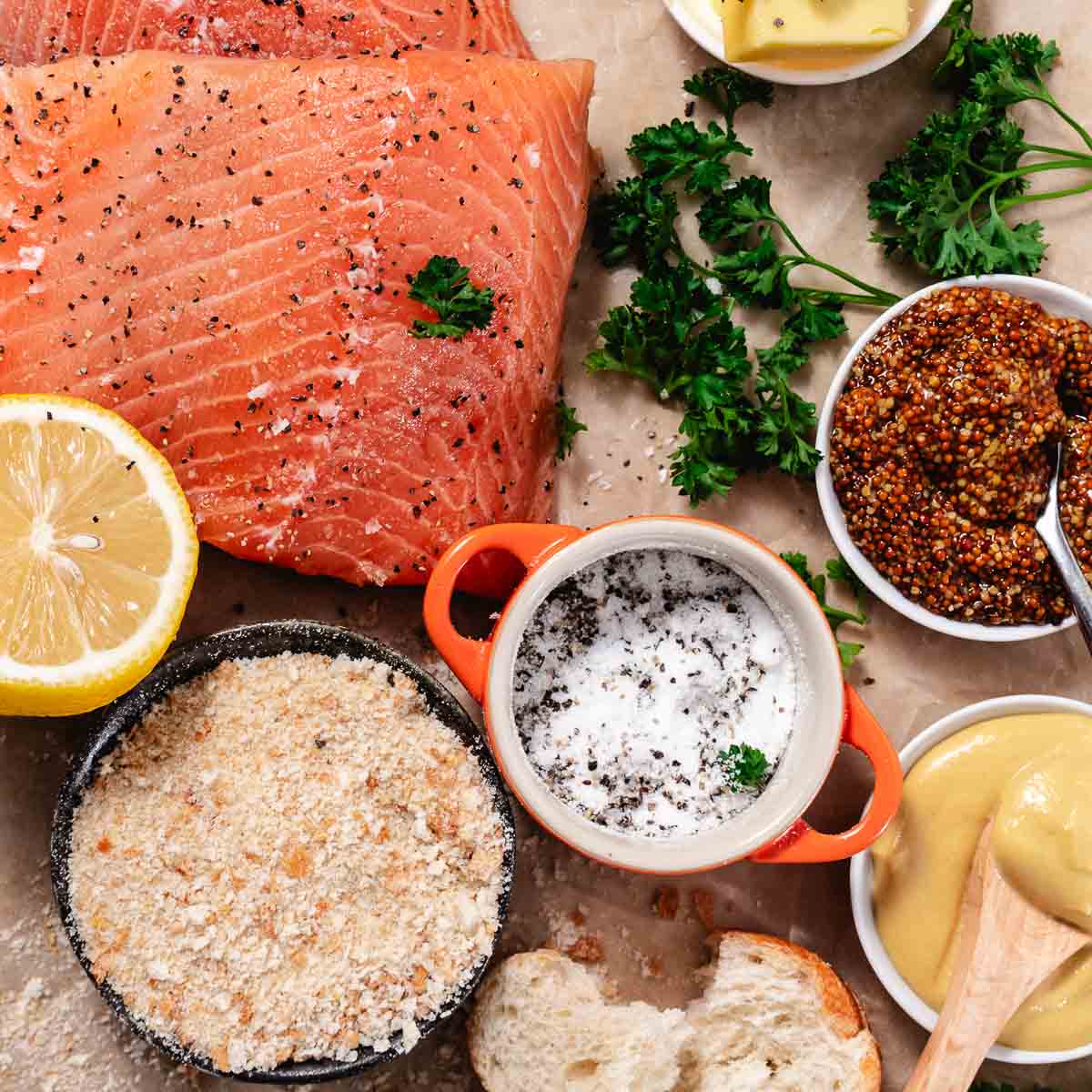 Ingredients for baked Dijon salmon including salmon fillet, whole grain mustard, breadcrumbs, lemon, butter, and fresh parsley.