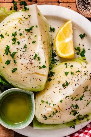 Tender boiled cabbage wedges seasoned with parsley and black pepper, served with olive oil and lemon.