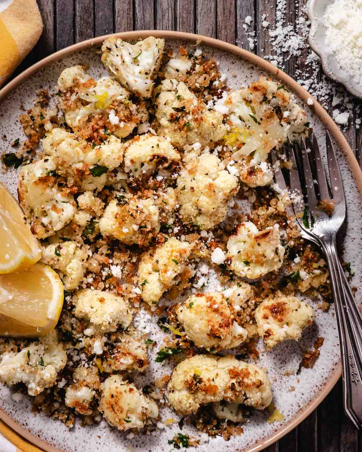 Raw cauliflower florets with olive oil, butter, lemon, breadcrumbs, herbs, salt, and cheese arranged on a plate.