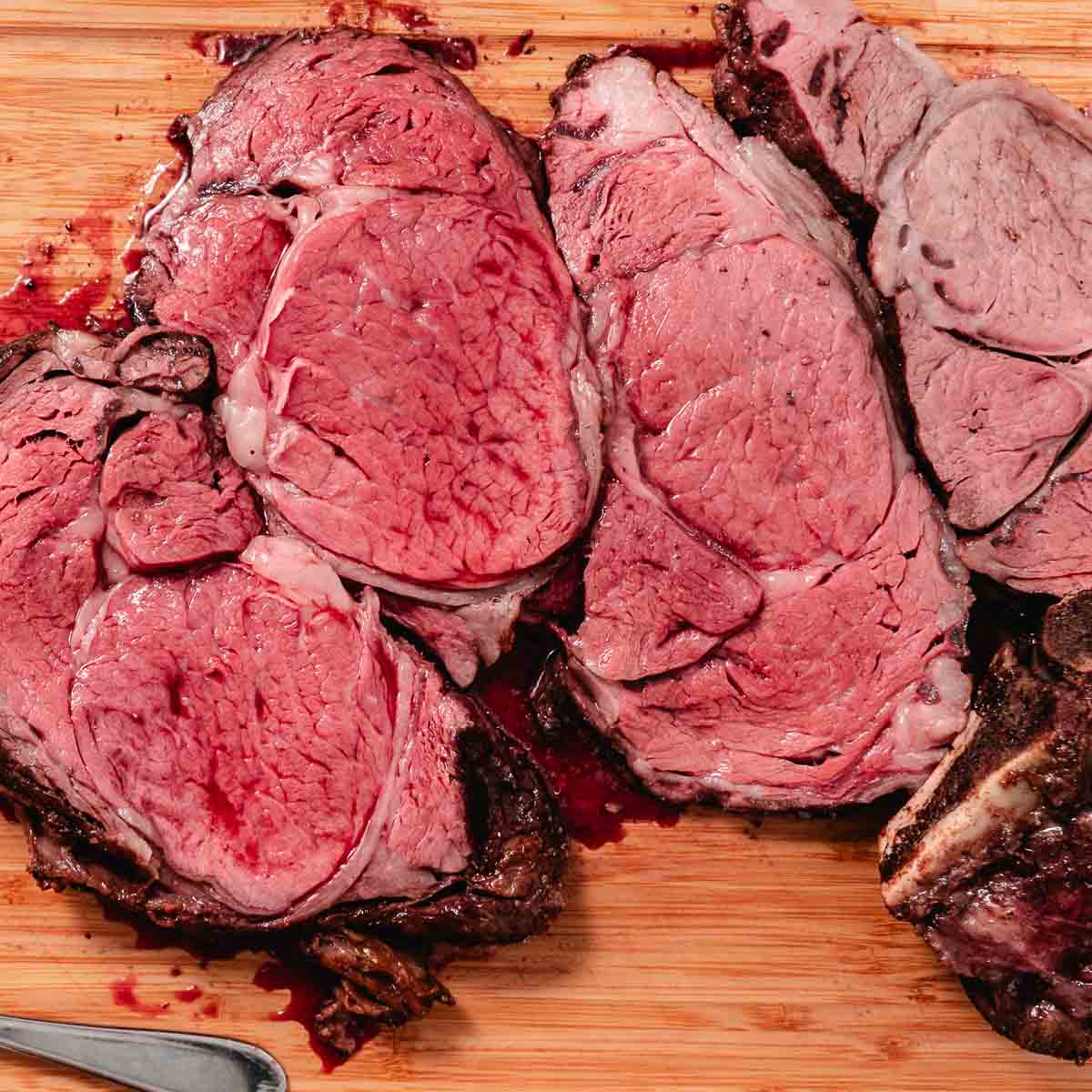 Sliced standing rib roast on a cutting board, showing medium-rare to medium doneness with a browned crust and juicy interior.