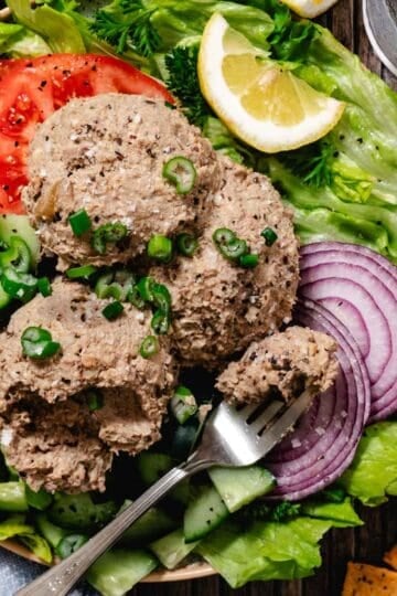 Close-up of chopped liver scoops topped with green onions, served on a fresh salad with cucumbers and red onion.