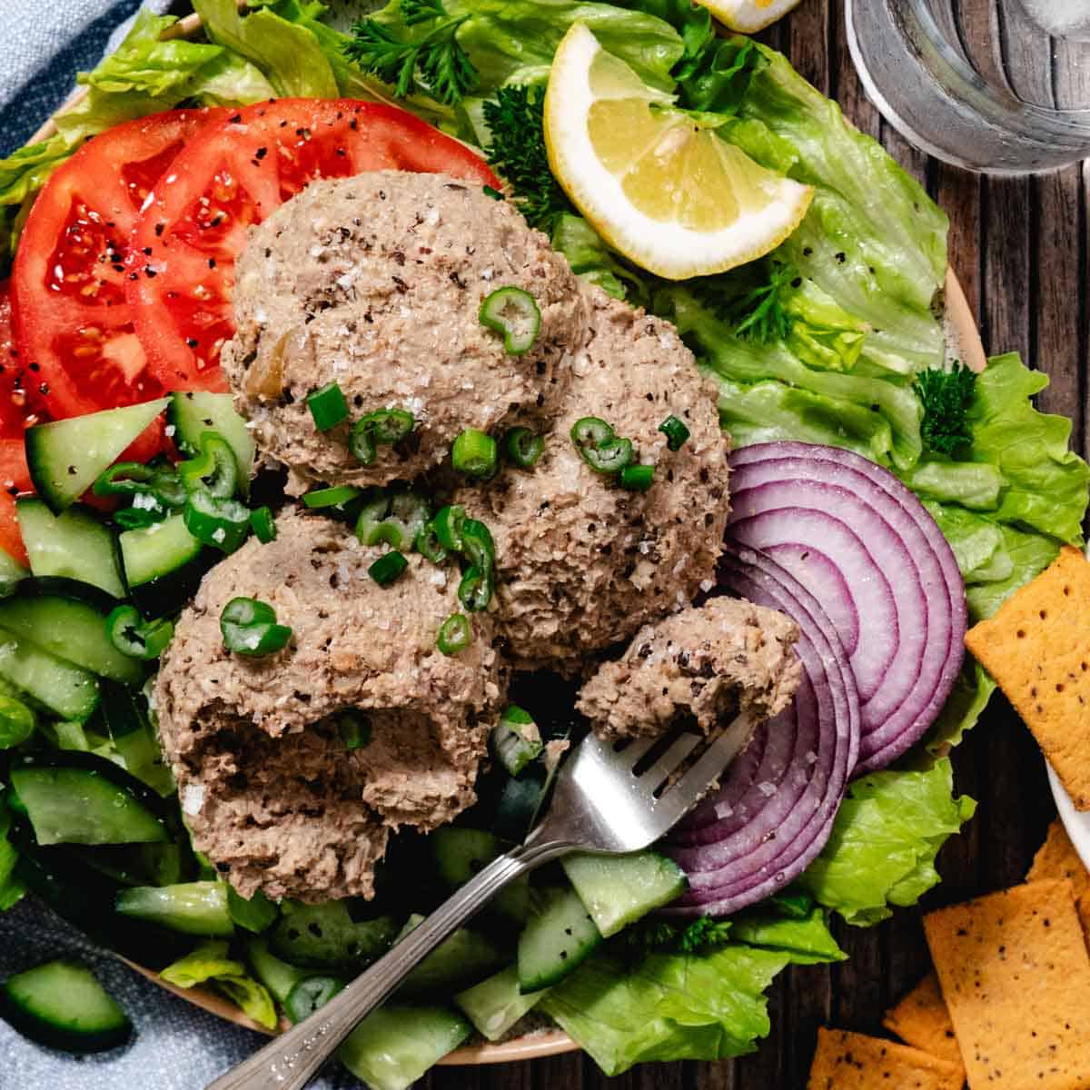 Close-up of chopped liver scoops topped with green onions, served on a fresh salad with cucumbers and red onion.
