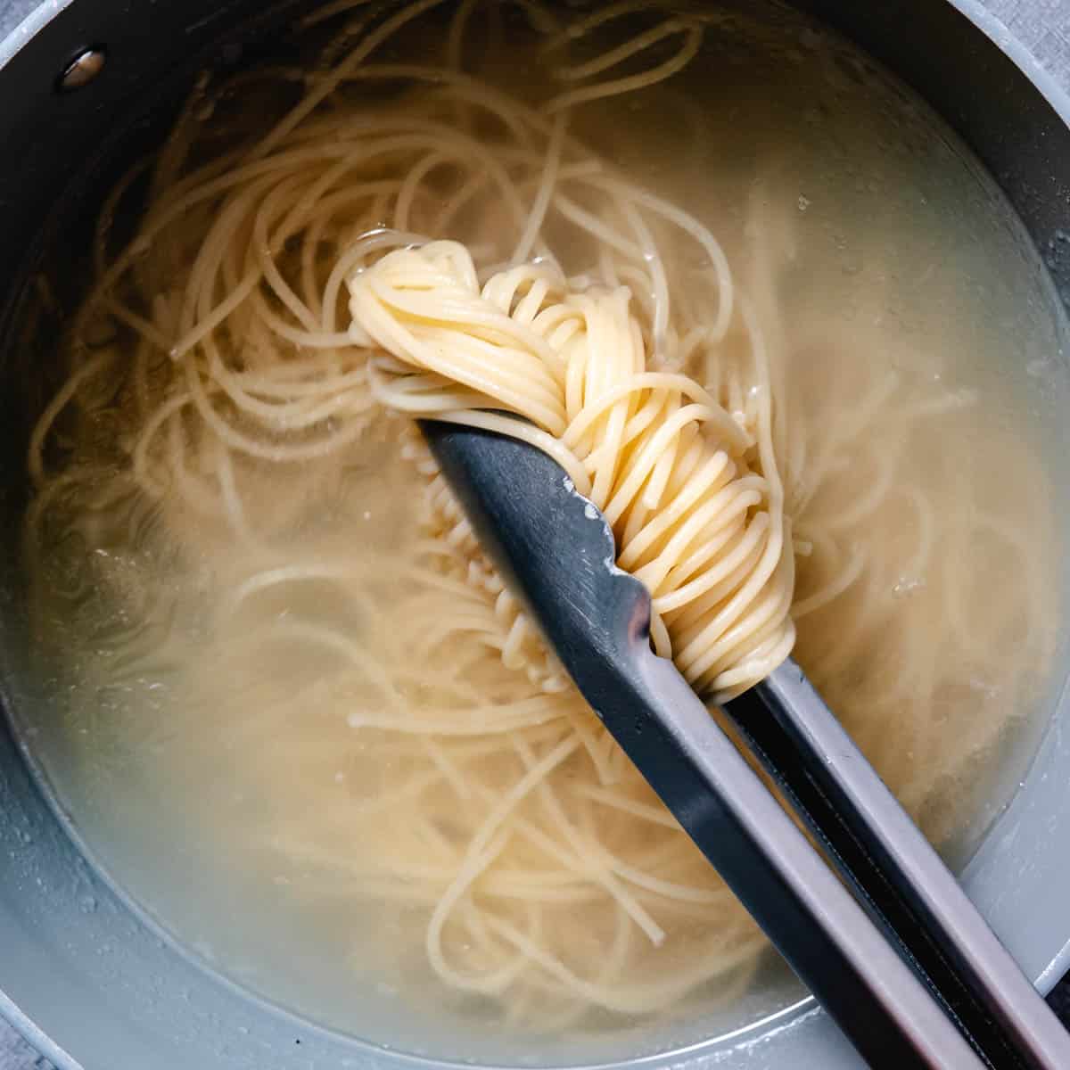 Spaghetti cooking in boiling water and lifted with kitchen tongs.