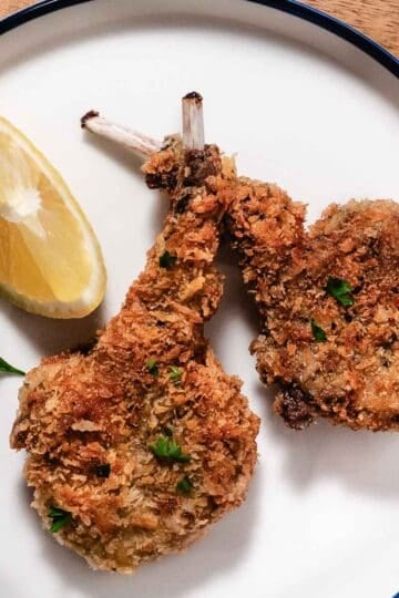 Golden panko breaded lamb chops plated with lemon and fresh parsley.
