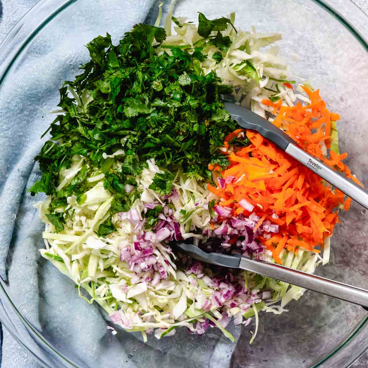 Shredded cabbage, grated carrot, diced red onion, and fresh cilantro in a glass bowl for mango coleslaw.