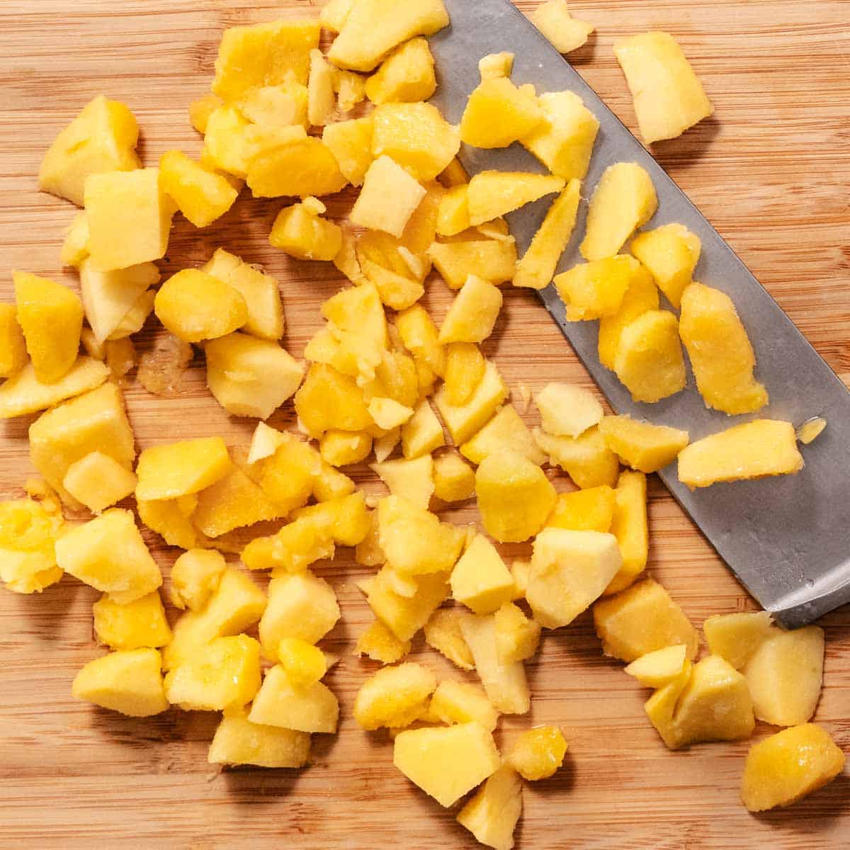 Diced frozen mango on a cutting board next to a chef’s knife.
