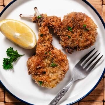 fried breaded lamb chops with a lemon wedge, parsley and a fork