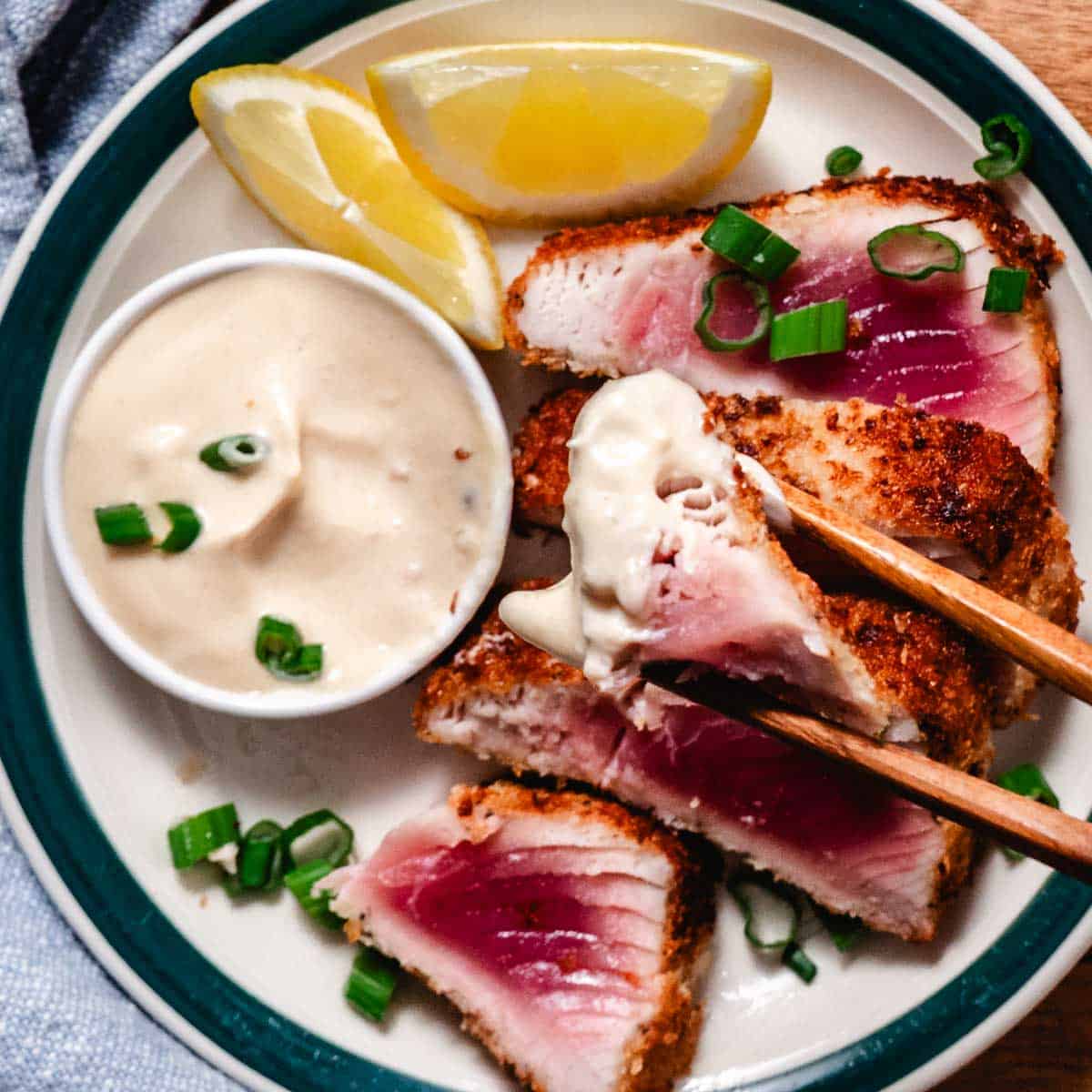 Panko crusted tuna steak dipped in creamy sauce, sliced with rare pink center and topped with green onions and lemon wedges.
