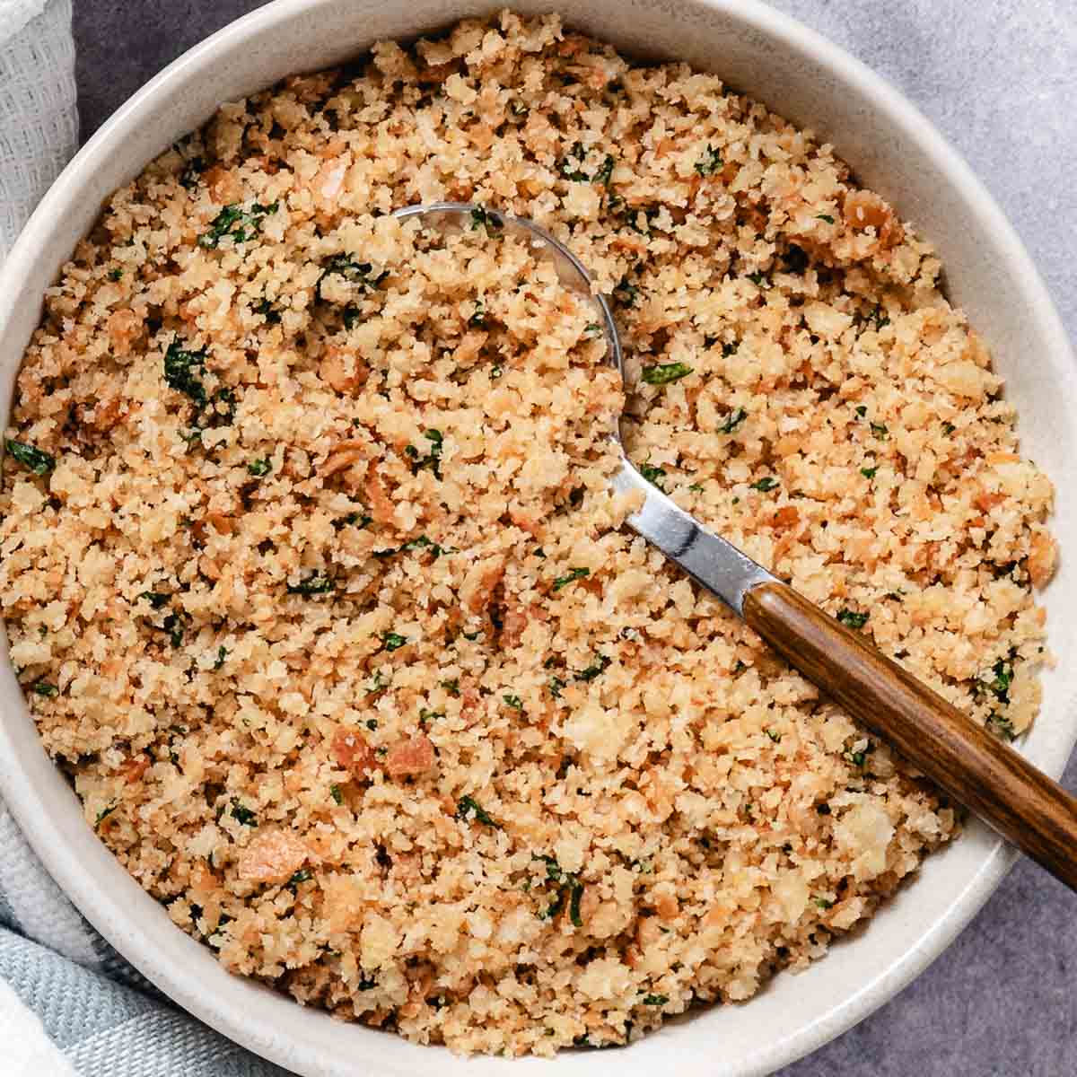 Buttery toasted breadcrumbs with parsley in a bowl with a spoon.