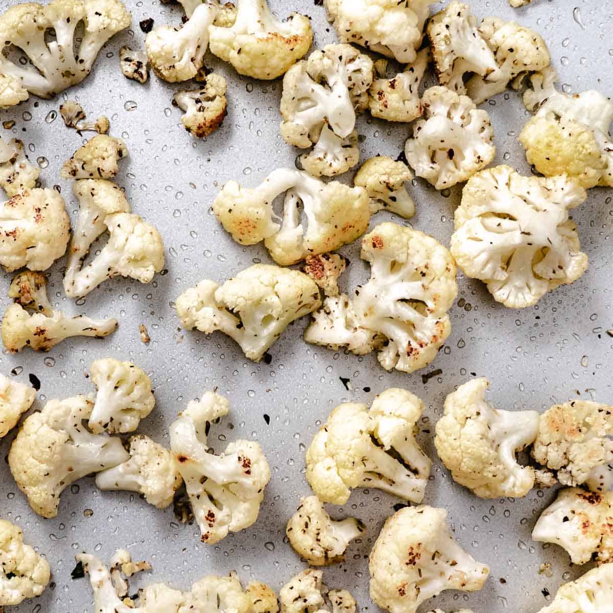 Seasoned roasted cauliflower florets with lightly browned edges on a sheet pan.