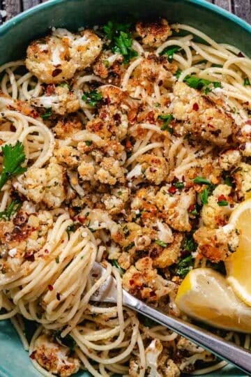 Roasted cauliflower pasta with spaghetti, buttery breadcrumbs, Parmesan cheese, parsley, red pepper flakes, and lemon wedges served in a bowl.