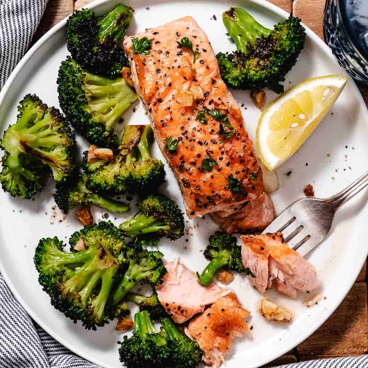 Lemon garlic seared salmon served with roasted broccoli and a lemon wedge on a white plate.