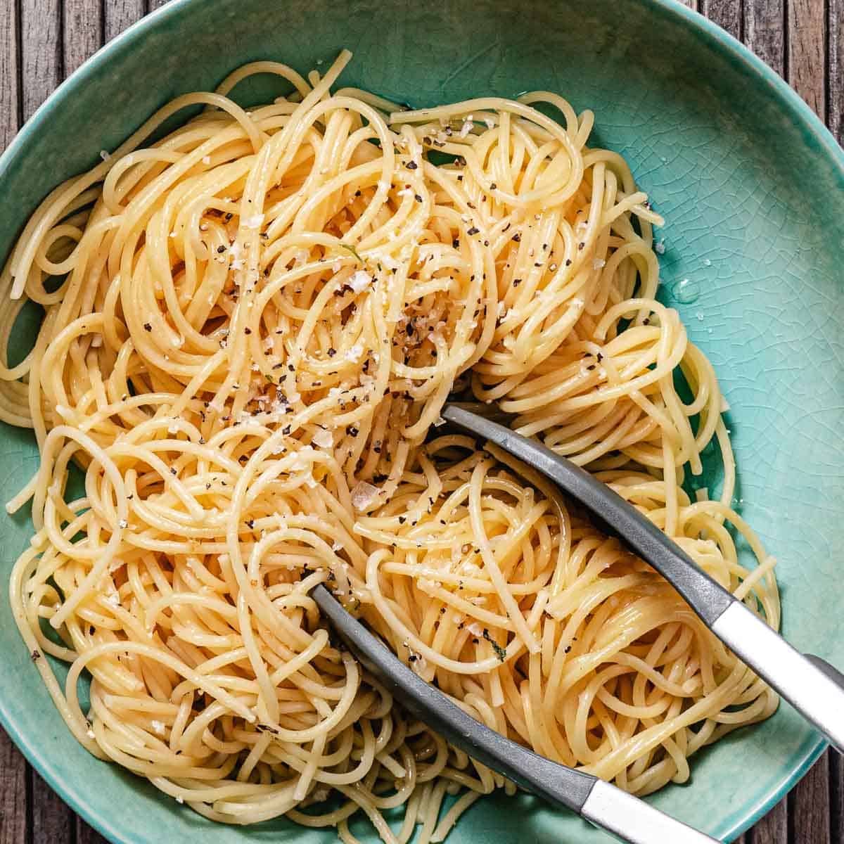 Cooked spaghetti tossed with salt and black pepper in a green bowl.