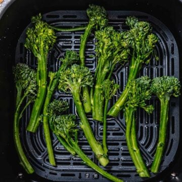 seasoned broccoli spears in air fryer basket before cooking