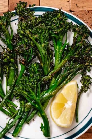 Air fryer broccolini with charred edges on a plate, finished with lemon wedge and seasoning
