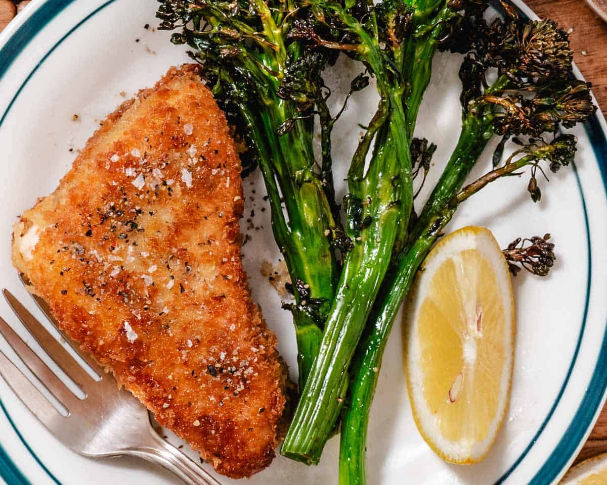 Crispy fish and and cooked broccolini with a lemon wedge on a plate.