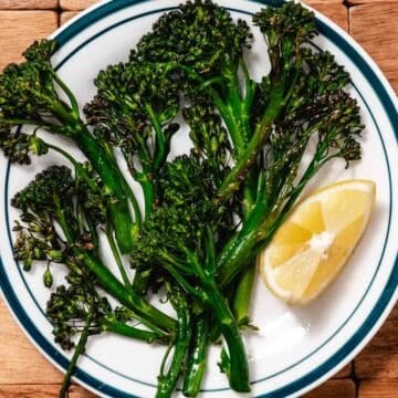 Air fryer broccolini with crispy edges on a plate with lemon wedge