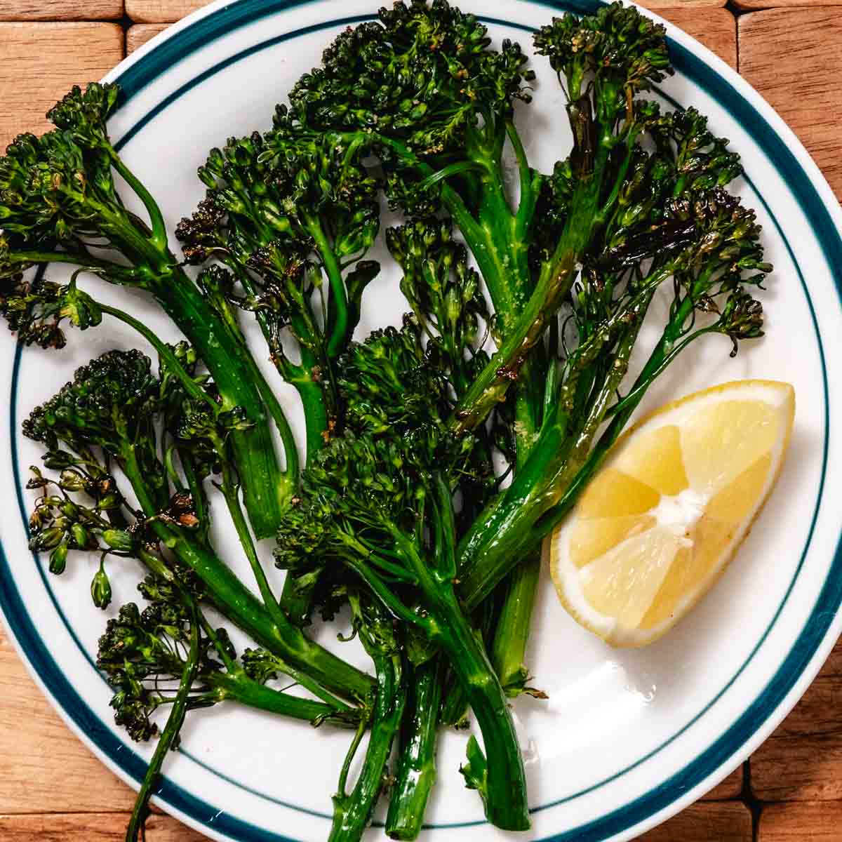 Air fryer broccolini with crispy edges on a plate with lemon wedge