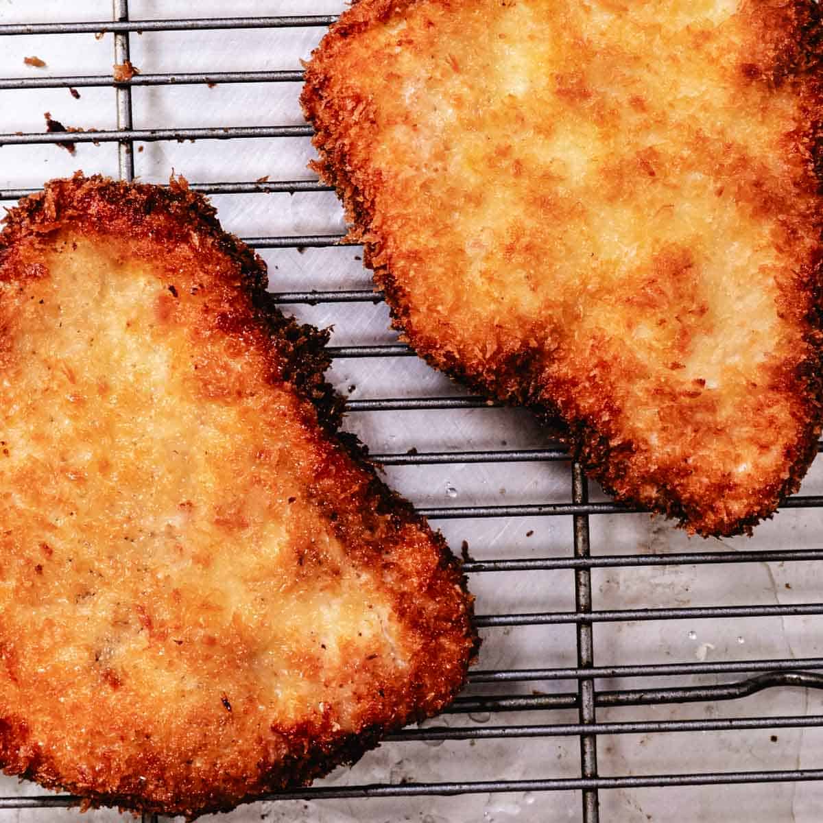 Chicken Milanese cutlets resting on a wire rack after frying 