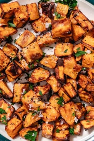Air fryer sweet potato cubes with browned edges, finished with salt, black pepper, and fresh herbs on a plate.
