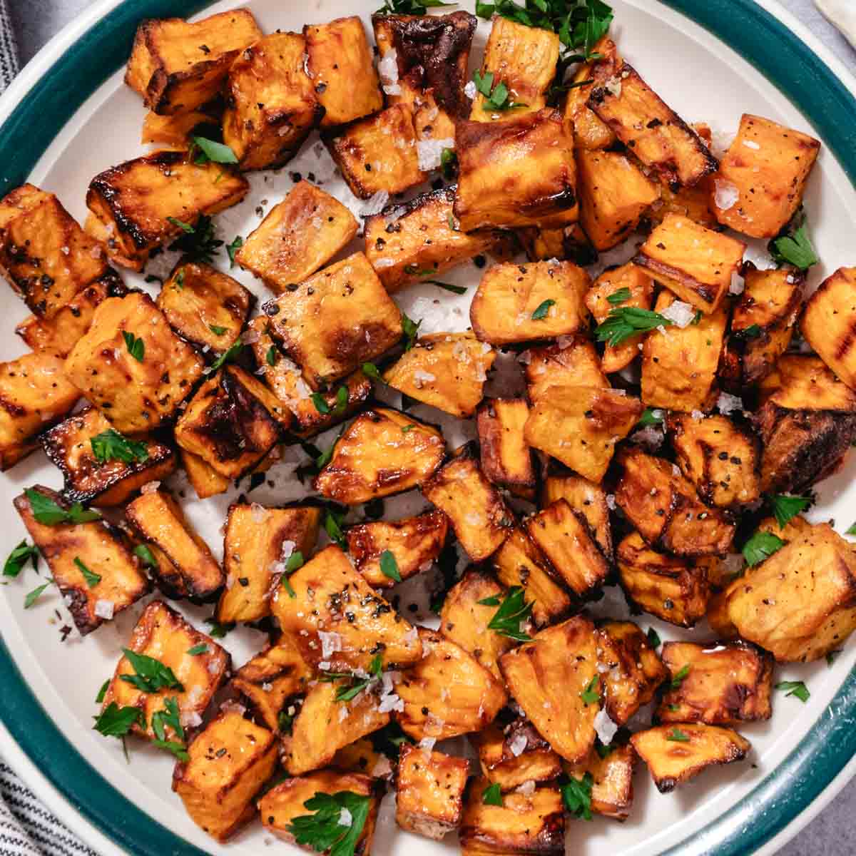 Air fryer sweet potato cubes with browned edges, finished with salt, black pepper, and fresh herbs on a plate.