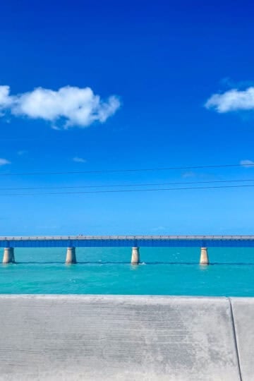 Overseas Highway bridge stretching across turquoise water in the Florida Keys under a bright blue sky with scattered clouds.