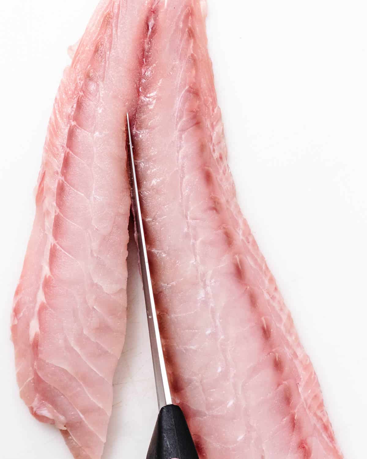 Knife cutting a fresh tilefish fillet down the center to remove the bone line.