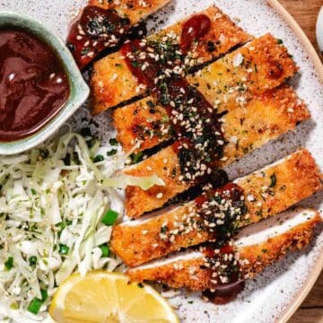 Japanese chicken katsu with crispy panko breading, sliced and served with tonkatsu sauce, cabbage slaw, and sesame seeds