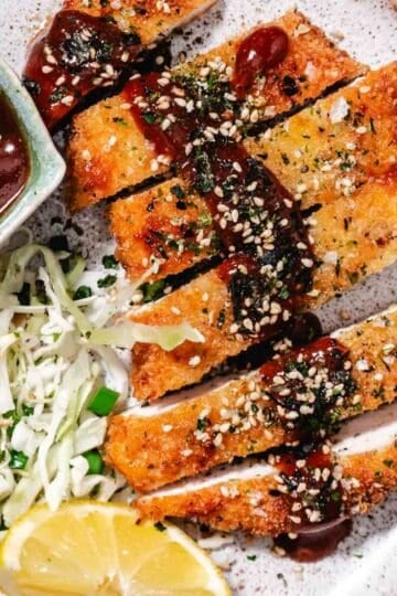 Japanese chicken katsu with crispy panko breading, sliced and served with tonkatsu sauce, cabbage slaw, and sesame seeds