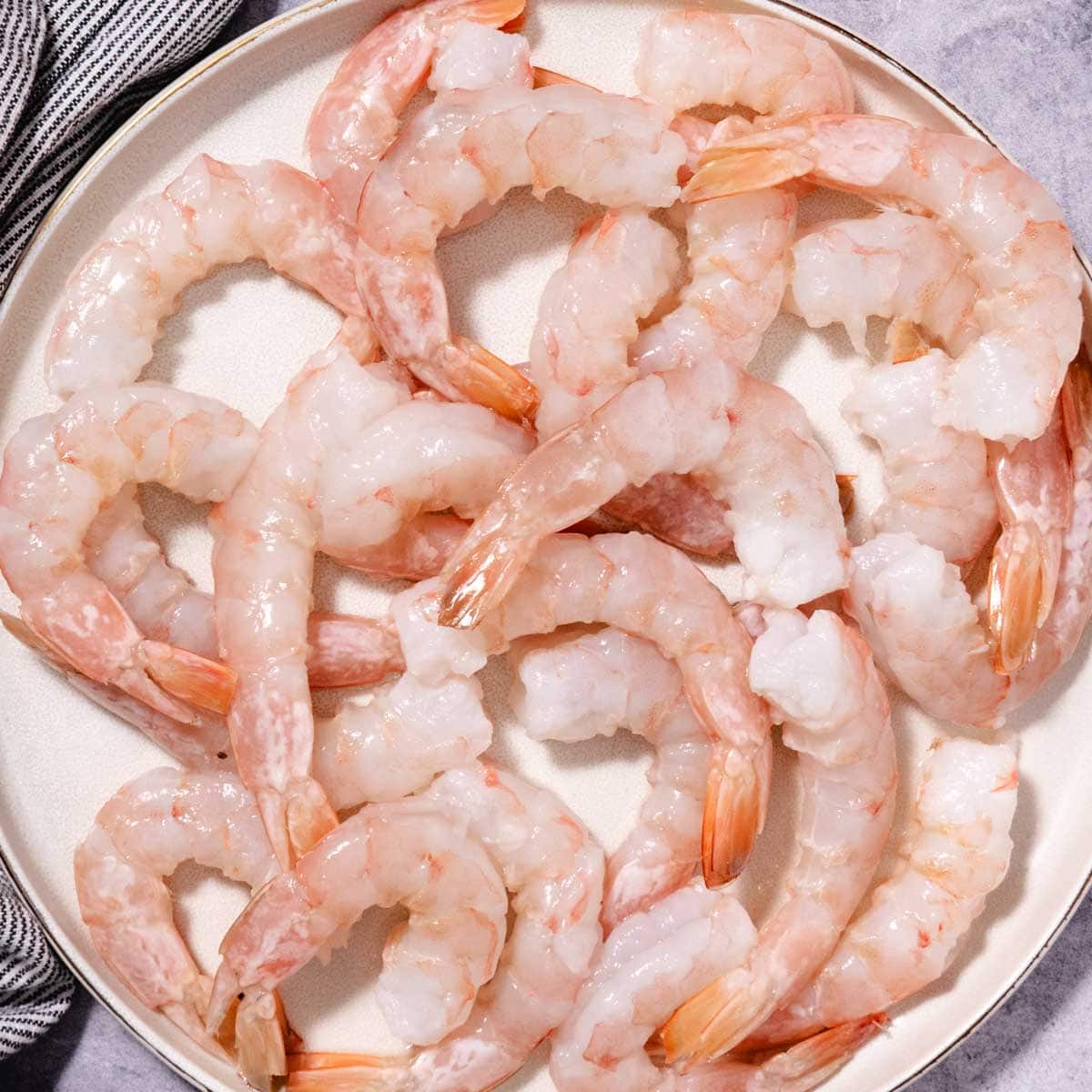 Raw Key West pink shrimp, peeled and deveined with tails on, arranged on a plate.