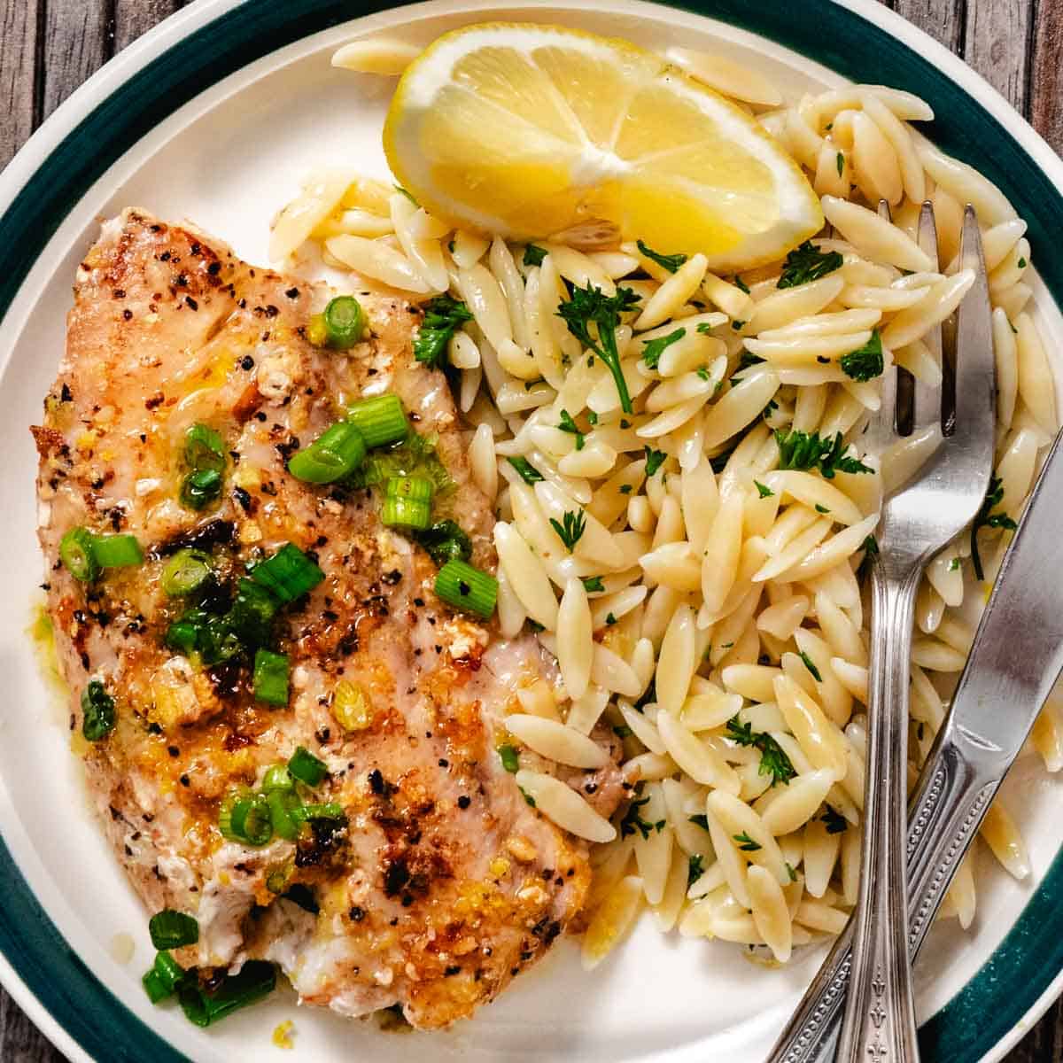Pan seared tilefish with lemon butter, green onions, and orzo pasta on a dinner plate.