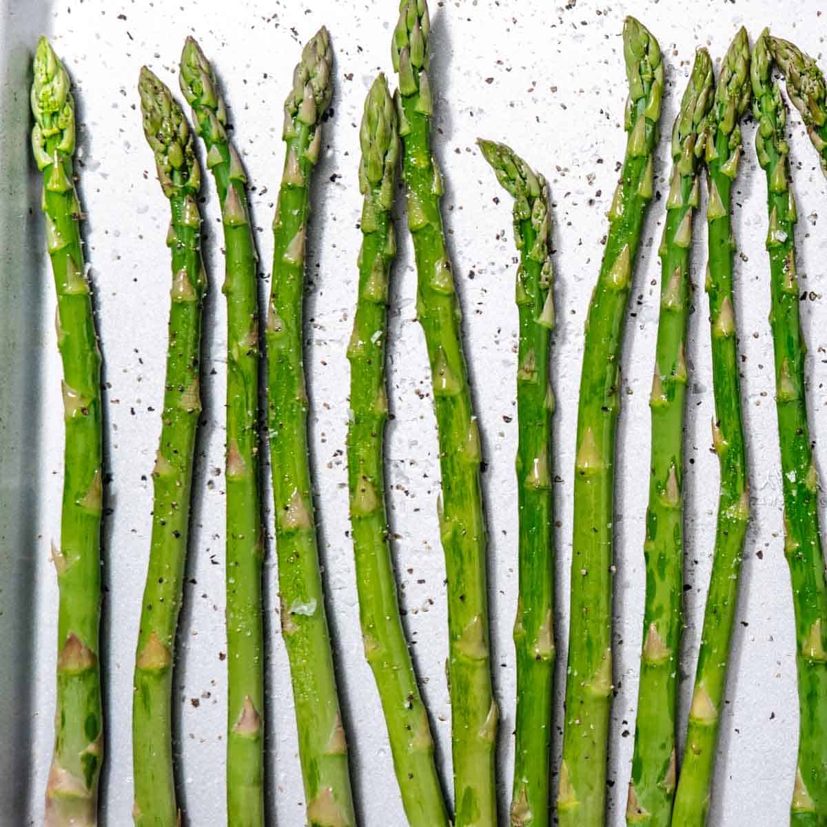 raw asparagus on sheet pan with oil salt and pepper