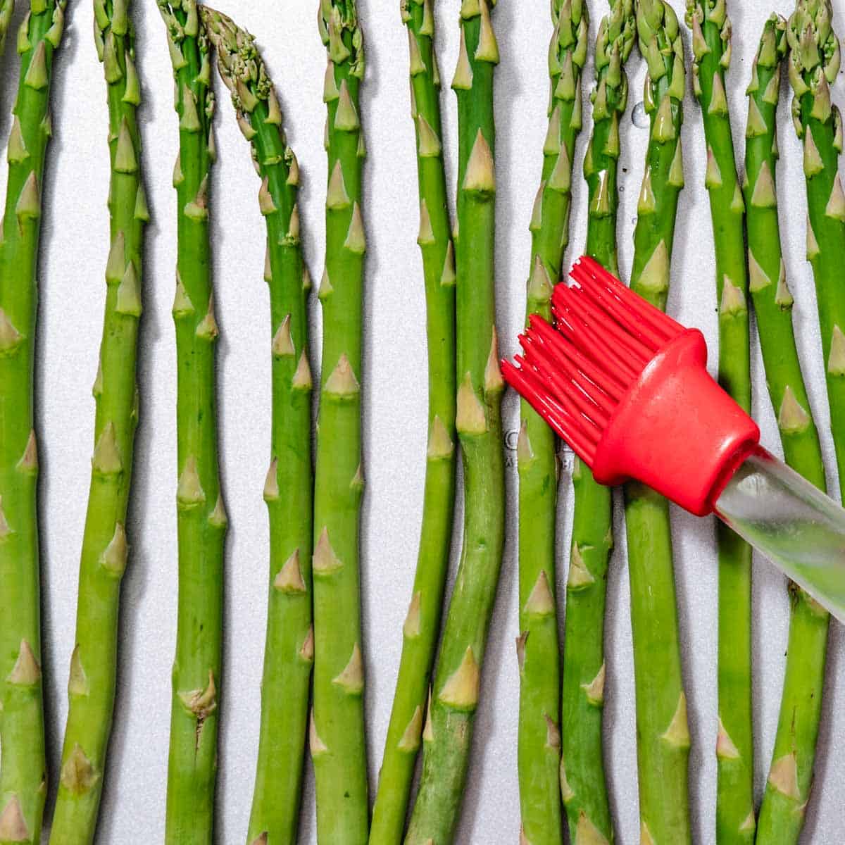 brushing oil onto asparagus on sheet pan before roasting