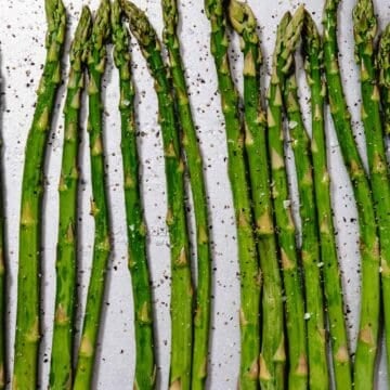 raw asparagus on sheet pan with oil, salt and black pepper