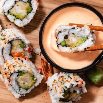 Shrimp tempura sushi roll dipped in spicy mayo with chopsticks over a wooden board