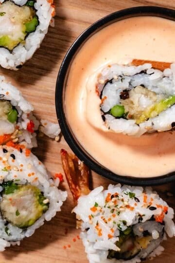 Shrimp tempura sushi roll dipped in spicy mayo with chopsticks over a wooden board