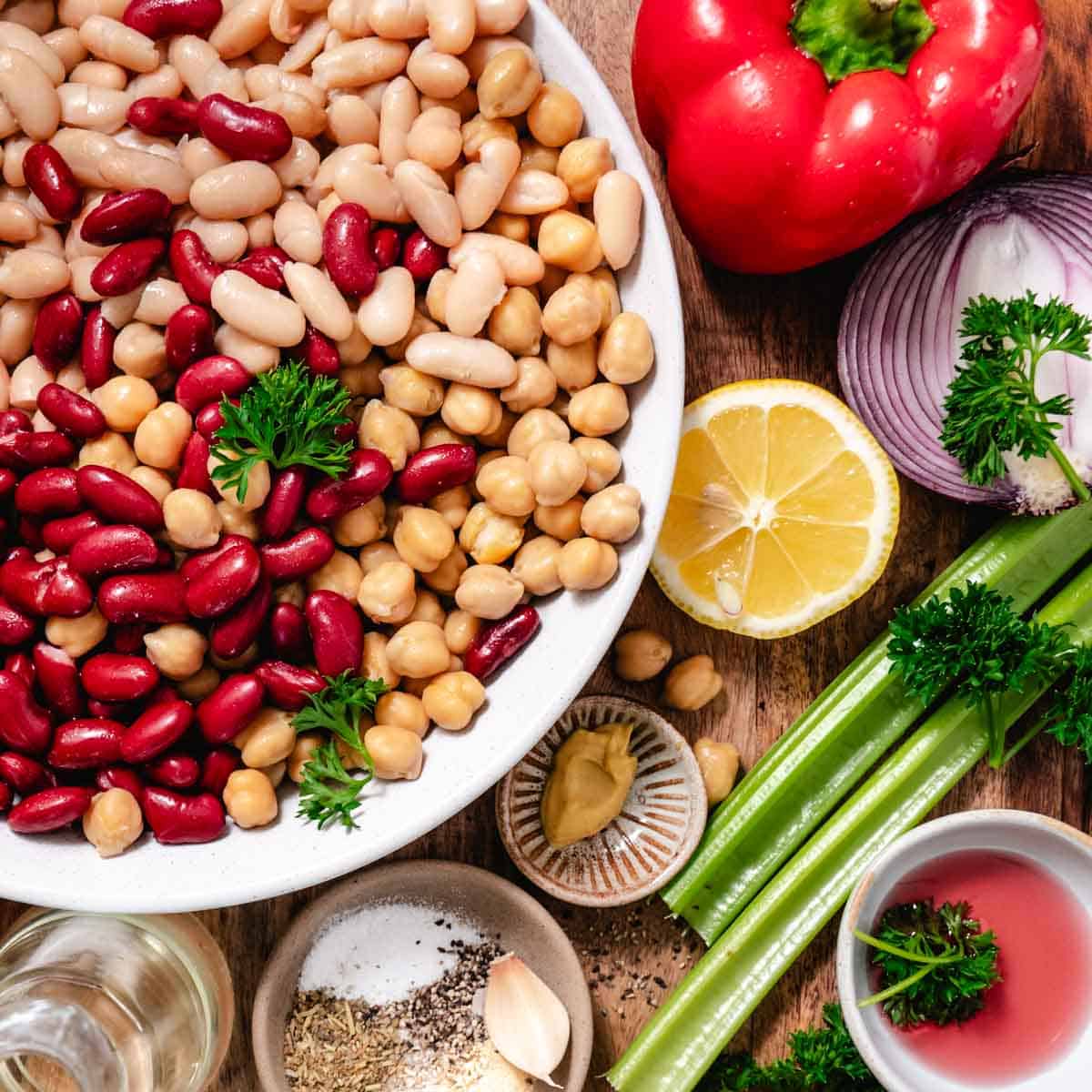 ingredients for 3 bean salad including chickpeas, kidney beans, white beans, celery, red onion, lemon, and herbs