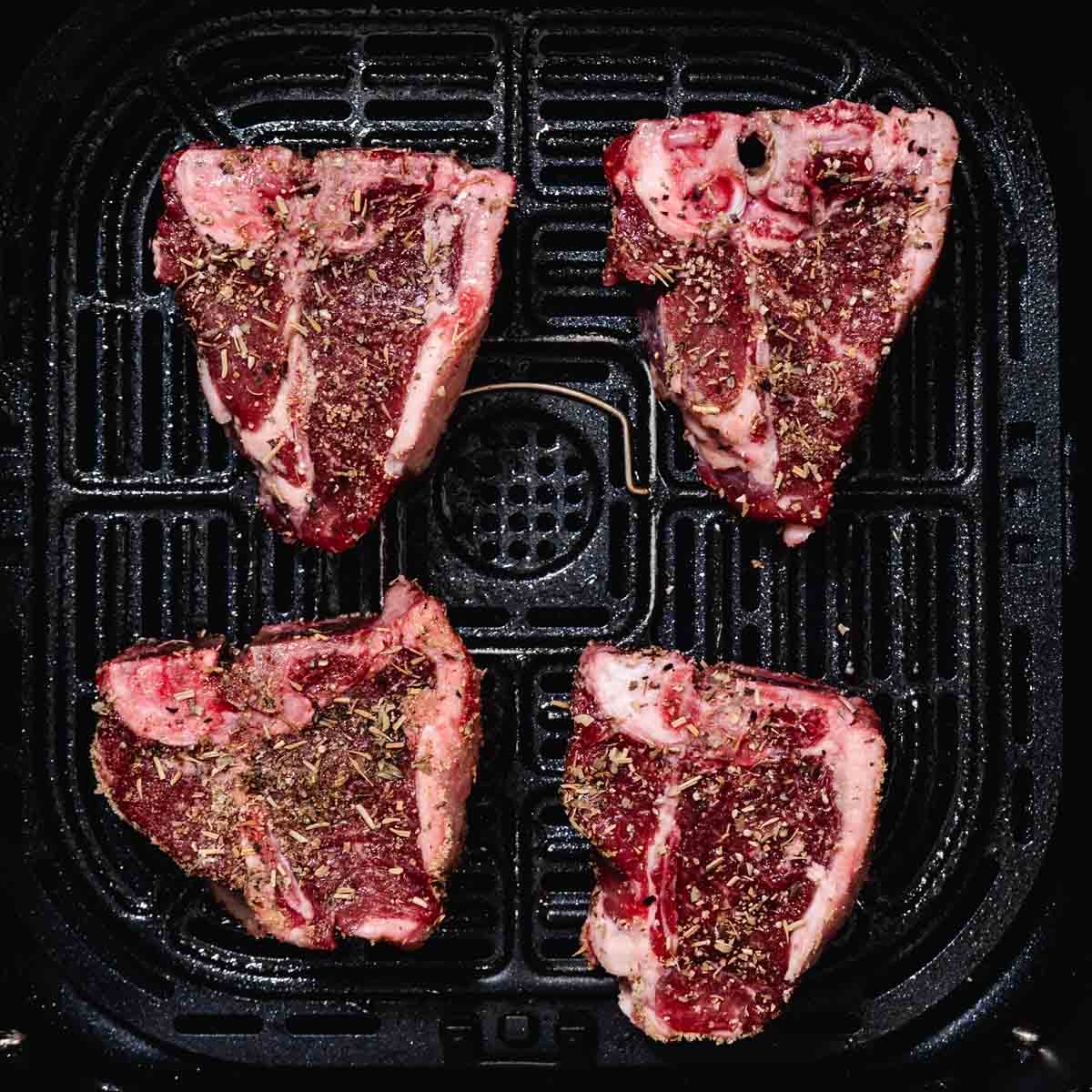 Air fryer basket with seasoned lamb loin chops before cooking